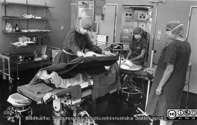 Förberedelse för operation i Lund
Brun ringbunden mjuk pärm, kirurgiska kliniken i Lund. På en operationssal. En sterilklädd operationssköterska dukar upp sterilt på den sövda patienten. En narkossköterska sitter vid huvudänden och ett icke sterilklätt biträde står beredd att assistera osterilt. Foto
Nyckelord: Lasarettet;Lund;Universitetssjukhuset;USiL;Operationsavdelningen;Kirurgisk;Kliniken