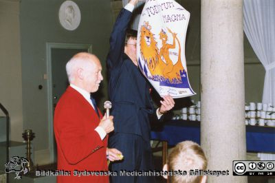 Philip Sandblom-symposium 1993 i Lund
Docent Stig Radner med en av honom ritad affisch som han presenterade vdi symposiebanketten i Universitetets Pelarsal. Foto.
Nyckelord: Lasarettet;Lund;Universitetssjukhuset;USiL;Kirurgiska;Kliniken;Symposium;Möte;Bankett;Fest