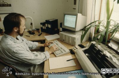 En typisk arbetssituation för en administratör år 1988
Datorn har en med den tidens mått en rätt stor katodstråleröres-skärm i en stor låda, och skärmen har nu ljus bakgrund. Själva datorlådan är försedd med 2 fack för utbytbara hårdskivor (varav en sitter i). Till höger om datorlådan sitter en extern CD-läsare. Skrivaren är en stor s.k. nålmatrisskrivare av mycket högljudd typ. Sådana fick snart byggas in i ljuddämpande lådor. Mellan datorn och skrivaren skymtar man en telefon (modell Ellemtel Diavox).
Nyckelord: Lasarettet;Lund;Universitetssjukhuset;USiL;Administration;Dator