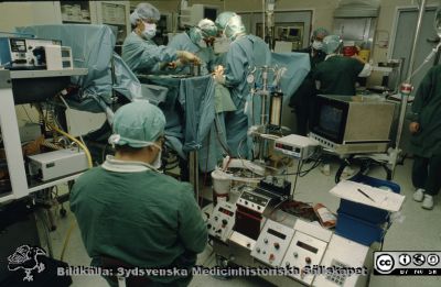 Rimligen en by-pass-operation på hjärta, troligen 1980 - 1990-talen i Lund
Närmast kameran en hjärt-lungmaskin med operatör, bortom honom hjärtoperatörerna och längst bort de kirurger som tar blodkärl från patientens ena ben.
Nyckelord: Lasarettet;Lund;Universitetssjukhuset;USiL;Thoraxkirurgiska, Kliniken;Bypass