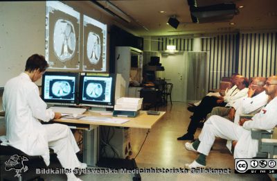 En röntgenrond i Lund i slutet på 1990-talet
Röntgenrond med kirurger i slutet på 1990-talet ledd av överläkaren, docent Kerstin Lyttkens med två stora monitorer framför sig. Bilderna (datortomografiska tvärsnitt genom patientens bål) projiceras på väggen för diskussion och samråd med och mellan de andra läkarna.
De svenska röntgenronderna har alltid varit viktiga centra för den kliniska verksamheten, och kommer rimligen att så förbli, alla förändringar i undersöknings- och presentationstekniker till trots.
Nyckelord: Lasarettet;Lund;Universitetssjukhuset;USiL;Röntgendiagnostiska;Kliniken
