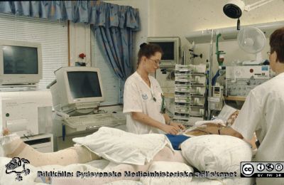 NIVA (neurologisk intensivvårdsavdelning)
Ur låda med blandade diabilder från sjukhusfotograferna i Lund, 1970-, 1980- och 1990-talen. Datorskärmarna ser ut som på 1990-talet. 
Manlig patient med gipsade ben, i respirator och många sladdar kopplade, kanske vård efter ett olycksfall.
Nyckelord: Lasarettet;Lund;Universitetssjukhuset;USiL;Neurologisk;Intensivvård;NIVA