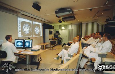 En röntgenrond i Lund i slutet på 1990-talet
Röntgenrond md kirurger i slutet på 1990-talet ledd av röntgenöverläkaren, docent Kerstin Lyttkens med två stora monitorer framför sig. Bilderna (datortomografiska tvärsnitt genom patientens bål) projiceras på väggen för diskussion och samråd med och mellan de andra läkarna.
De svenska röntgenronderna har alltid varit viktiga centra för den kliniska verksamheten, och kommer rimligen att så förbli, alla förändringar i undersöknings- och presentationstekniker till trots.
Nyckelord: Lasarettet;Lund;Universitetssjukhuset;USiL;Röntgendiagnostiska;Kirurgiska