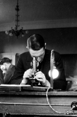 1928 års kurs i histologi i Lund
Fotoalbum märkt Histologikursen anno 1928. 
Detta album innehåller bilder från dåvarande histologiska avdelningen på anatomiska institutionen i Lund på Biskopsgatan 7. Liksom de övriga i serien skapades det av kursdeltagarna och tillägnades kursledaren professor Torsten Hellman som uppskattning av hans lärargärning. Bildtext  "De långe - Assar Olsson". Student vid kursmikroskop.
Bildkälla Stiftelsen Locus Medicus Lundensis 250317.
Nyckelord: Locus Medicus Lundensis;Medicinska fakulteten i Lund;Histologiska avdelningen;Sydsvenska Medicinhistoriska Sällskapet;SMHS;Anatomiska Institutionen;Studenter