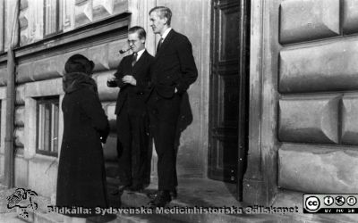 Fotoalbum tillägnat Professor Torsten Hellman 1929.
Fotoalbum tillägnat Professor Torsten Hellman med tacksamhet och vördnad från histologikursen 1929. Bildtext saknas. Rimligen medicine studerande på histologiska avdelningen vid entrén till anatomiska institutionen i Lund.  De båda unga männen har inomhuskläder, men kvinnan har varma utomhuskläder och pälsbrämad mössa och krage. Foto alltså i svalt väder.
Bildkälla Stiftelsen Locus Medicus Lundensis 250317. Fotograf okänd.
Nyckelord: Anatomiska Institutionen;Histologiska avdelningen;Mikroskoperingssal;Lärare;Locus Medicus Lundensis;Medicinska fakulteten i Lund