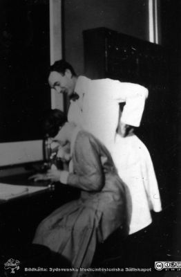 Fotoalbum tillägnat professor Torsten Hellman från histologikursen HT 1930
Fotoalbum "TILL PROFESSOR TORSTEN HELLMAN MED TACK FRÅN DELTAGARNA I HISTOLOGIKURSEN HÖSTTERMINEN 1930". Bildtext "Undervisning, Krisch". Kanske kursamanuensen Christiansen vid en kvinnlig student. 
Bildkälla stiftelsen Locus Medicus Lundensis och Sydsvenska Medicinhistoriska Sällskapet / SMHS. Fotograf okänd.
Nyckelord: Histologiska avdelningen;Anatomiska Institutionen;Entrétrappa;Medicinska fakulteten i Lund;Sydsvenska Medicinhistoriska Sällskapet;Locus Medicus Lundensis;Lärare