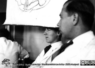 Fotoalbum från histologikursen i Lund 1931
Fotoalbum från histologikursen 1931. Bildtext "Jerre är intresserad men Lange - - ". Rimligen  amanuenserna Jerre och Lange i stora föreläsningssalen på anatomiska institutionen i Lund. 
Bildkälla Stiftelsen Locus Medicus Lundensis 250317. Sydsvenska Medicinhistoriska Sällskapet / SMHS. Fotograf okänd.
Nyckelord: -Medicine studerande;Histologiska avdelningen;Anatomiska Institutionen;Medicinska fakulteten i Lund;Locus Medicus Lundensis;Universitetet i Lund;Fföreläsningssal