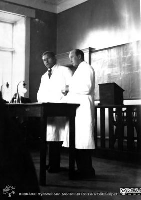 Fotoalbum från histologikursen i Lund 1931
Fotoalbum från histologikursen 1931. Bildtext "Vad månde dryftas? ". Okänd amanuens (Jerre eller Lange?) till vänster. Amanuens Gösta Glimstedt (1905 - 1970) till höger. Foto i stora föreläsningssalen på anatomiska institutionen i Lund. 
Bildkälla Stiftelsen Locus Medicus Lundensis 250317. Sydsvenska Medicinhistoriska Sällskapet / SMHS. Fotograf okänd.
Nyckelord: -Medicine studerande;Histologiska avdelningen;Anatomiska Institutionen;Medicinska fakulteten i Lund;Locus Medicus Lundensis;Universitetet i Lund;Föreläsningssal