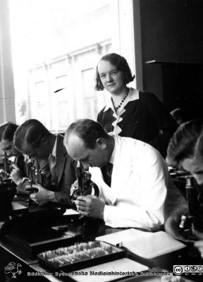 Fotoalbum från histologikursen i Lund 1931
Fotoalbum från histologikursen 1931. Bildtext "Arbetsflit ". Studenter vid sina mikroskop. En okänd amanuens hjälper studentskan bakom. Foto i mikroskoperingssalen på anatomiska institutionen i Lund. 
Bildkälla Stiftelsen Locus Medicus Lundensis 250317. Sydsvenska Medicinhistoriska Sällskapet / SMHS. Fotograf okänd.
Nyckelord: Medicine studerande;Histologiska avdelningen;Anatomiska Institutionen;Medicinska fakulteten i Lund;Locus Medicus Lundensis;Universitetet i Lund;Föreläsningssal