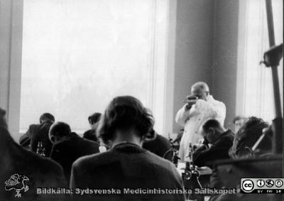 Fotoalbum  "Kursen i histologi V. T. 1933.
Fotoalbum "Kursen i histologi V. T. 1933. Bildtext: "Chefen docerar". Professor Torsten Hellman visar något med sina händer framför sitt ansikte för medicine studerande i histologiska avdelningens mikroskoperingssal på anatomiska institutionen i Lund. 
Bildkälla stiftelsen Locus Medicus Lundensis och Sydsvenska Medicinhistoriska Sällskapet / SMHS. Fotograf okänd.
Nyckelord: Locus Medicus Lundensis;Medicinska fakulteten i Lund;Histologiska avdelningen;Medicinska fakulteten i Lund;Sydsvenska Medicinhistoriska Sällskapet;Anatomiska Institutionen;Student
