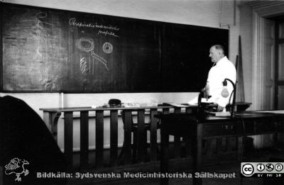 Fotoalbum  tillägnat Professor Torsten Hellman av lärjungarna 1935. Bildtextsaknas. Professor Hellman föreläser om ämnesomsättning och blodkärl för kursen med medicine studerande på avdelningen för histologi på anatomiska institutionen i Lund. 
Bildkälla stiftelsen Locus Medicus Lundensis och Sydsvenska Medicinhistoriska Sällskapet / SMHS. Fotograf okänd.
Nyckelord: Histologiska avdelningen;Anatomiska Institutionen;Sydsvenska Medicinhistoriska Sällskapet;Medicinska fakulteten i Lund;Locus Medicus Lundensis;Medicine studerande;Lunds universitet