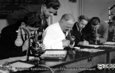 Fotoalbum  tillägnat Professor Torsten Hellman av lärjungarna 1935. Bildtext saknas. Professor Hellman hjälper studenterna i mikroskop. De ärmedicine studerande på avdelningen för histologi på anatomiska institutionen i Lund. 
Bildkälla stiftelsen Locus Medicus Lundensis och Sydsvenska Medicinhistoriska Sällskapet / SMHS. Fotograf okänd.
Nyckelord: Histologiska avdelningen;Anatomiska Institutionen;Sydsvenska Medicinhistoriska Sällskapet;Medicinska fakulteten i Lund;Locus Medicus Lundensis;Medicine studerande;Lunds universitet