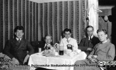 Fotoalbum tillägnat Professor Torsten Hellman med tacksamhet och vördnad från histologkursen 1929. Bildtext saknas. kaffefest på amanuensvåningen. Kanske en flaska Eau-de-Vie på bordet. Möjligen är det från vänster amanuenserna Fredrik Koch, Hjalmar Sjövall, okänd, Olof Ask och okänd vid bordet. Den okända längst till höger har ett träsvärd i knät  som hade han medverkat i ett spex.
Nyckelord: Anatomiska Institutionen;Histologiska avdelningen;Medicinska fakulteten i Lund;Locus Medicus Lundensis;Lunds universitet;Amanuensvåning;Konjak;Kaffekalas