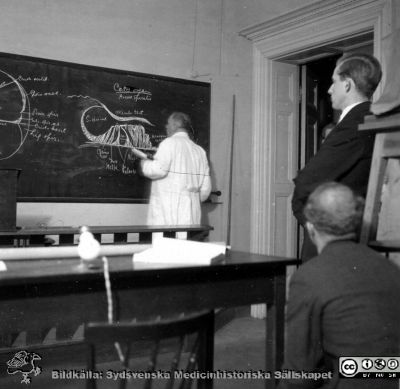 Fotoalbum "TILL PROFESSOR TORSTEN HELLMAN MED TACK FRÅN DELTAGARNA I HISTOLOGIKURSEN HÖSTTERMINEN 1930".  Bildtext "MOT SLUTET. Den oundvikliga fotografin från genomgåendet av örat."  Professor Torsten Hellman i institutionens stora föreläsningssal. 
Bildkälla stiftelsen Locus Medicus Lundensis och Sydsvenska Medicinhistoriska Sällskapet / SMHS. Fotograf okänd.
Nyckelord: Histologiska avdelningen;Anatomiska Institutionen;Medicinska fakulteten i Lund;Sydsvenska Medicinhistoriska Sällskapet;SMHS;Locus Medicus Lundensis;Elever;Lärare